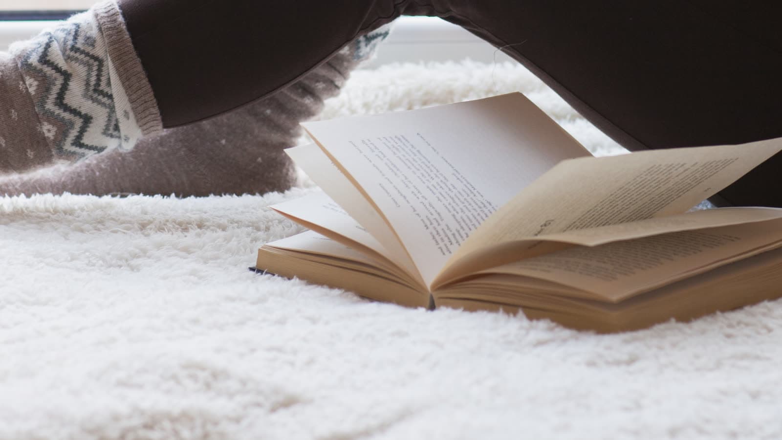 An open book rests on a blanket near a window.